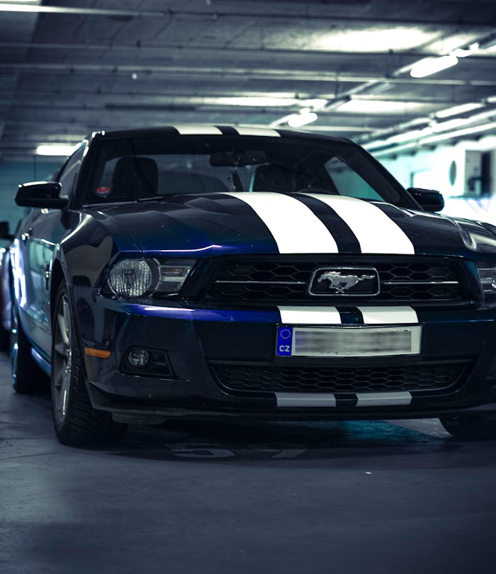 Primer plano de un Ford Mustang azul con franjas blancas estacionado en un garaje cubierto.